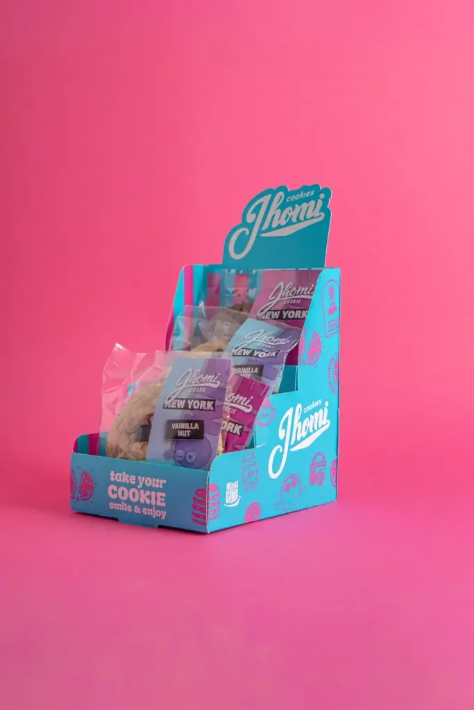 Exhibidor de Jhomi Cookies con paquetes de galletas sobre fondo rosa.