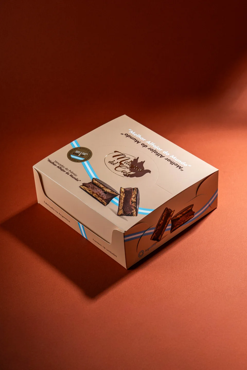 Caja cerrada de Milagros del Cielo con bandas celestes, imágenes de alfajores y logotipo dorado.